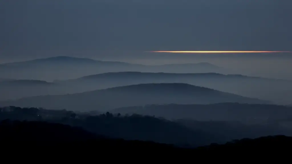 Layered ridgelines in blue fog at dusk with a thin gold band on the horizon
